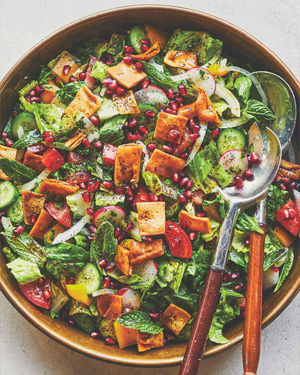 Une salade dans un bol de service brun, avec de la laitue, divers légumes et des morceaux de pita frit.