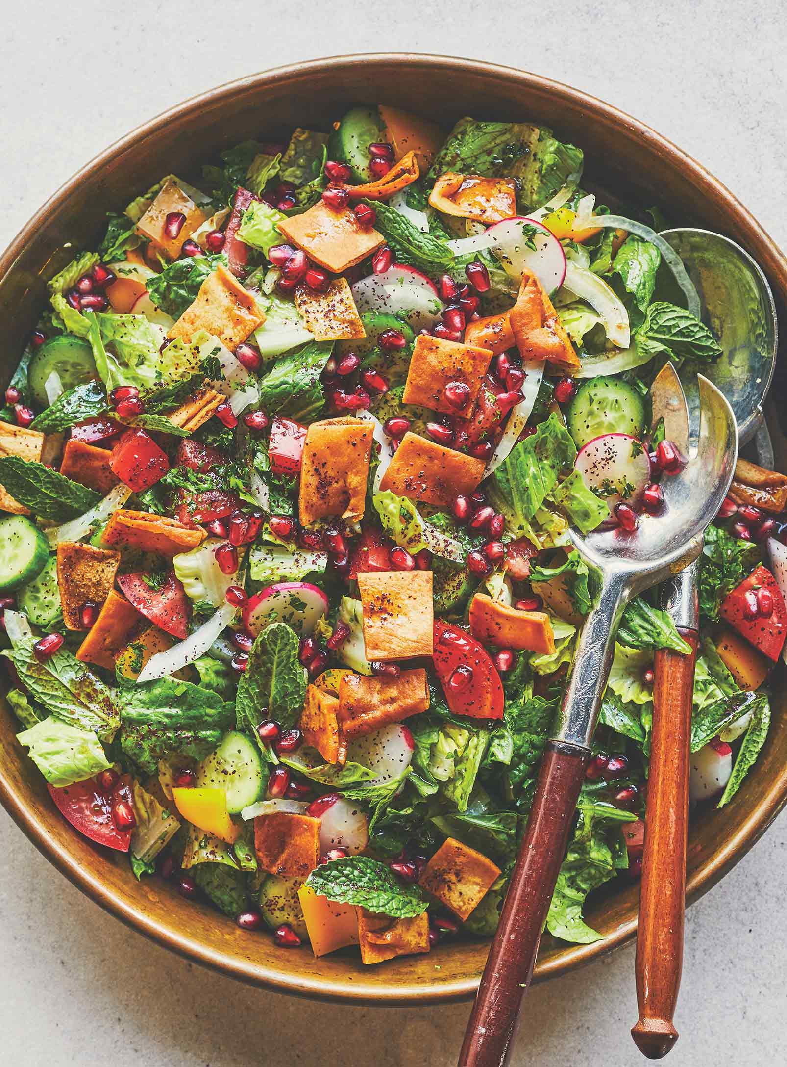 Une salade dans un bol de service brun, avec de la laitue, divers légumes et des morceaux de pita frit.