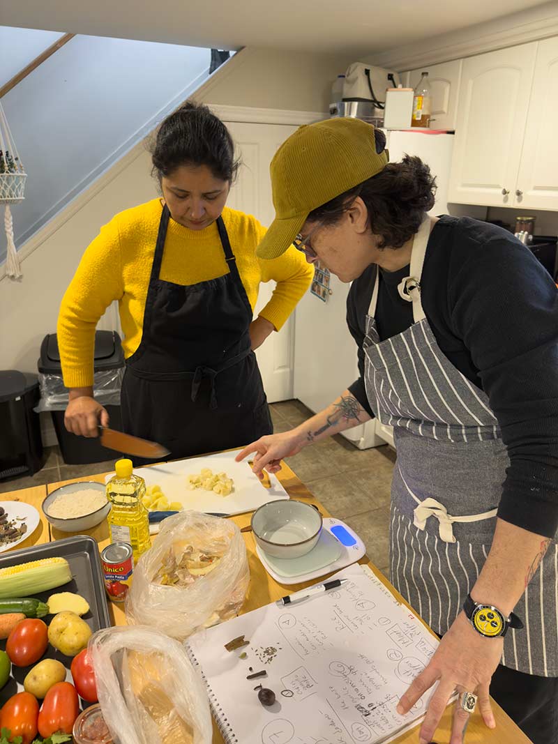 Elvira et Hina préparent des plats ensemble dans une cuisine, debout devant un comptoir avec des ingrédients et des ustensiles.