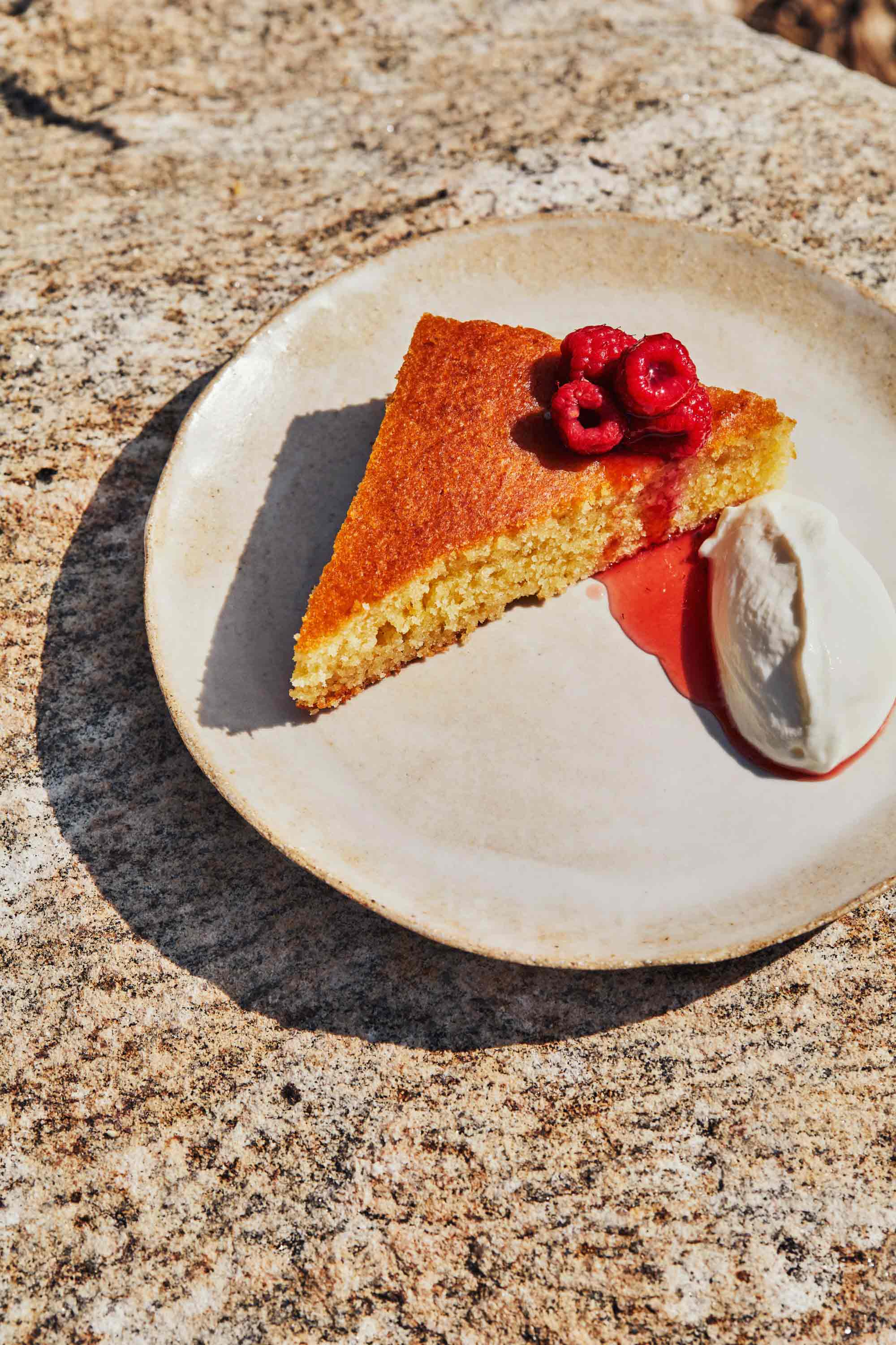 Un gâteau sur une assiette beige, garni d’une poignée de framboises sur le dessus et de crème fouettée au yogourt sur le côté.