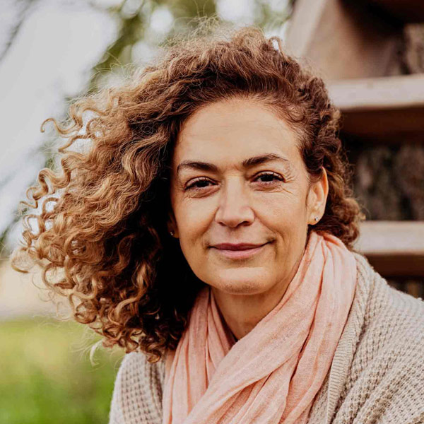 Portrait d’une femme turque souriante, les cheveux bouclés sur le côté, portant un foulard rose et un cardigan beige.