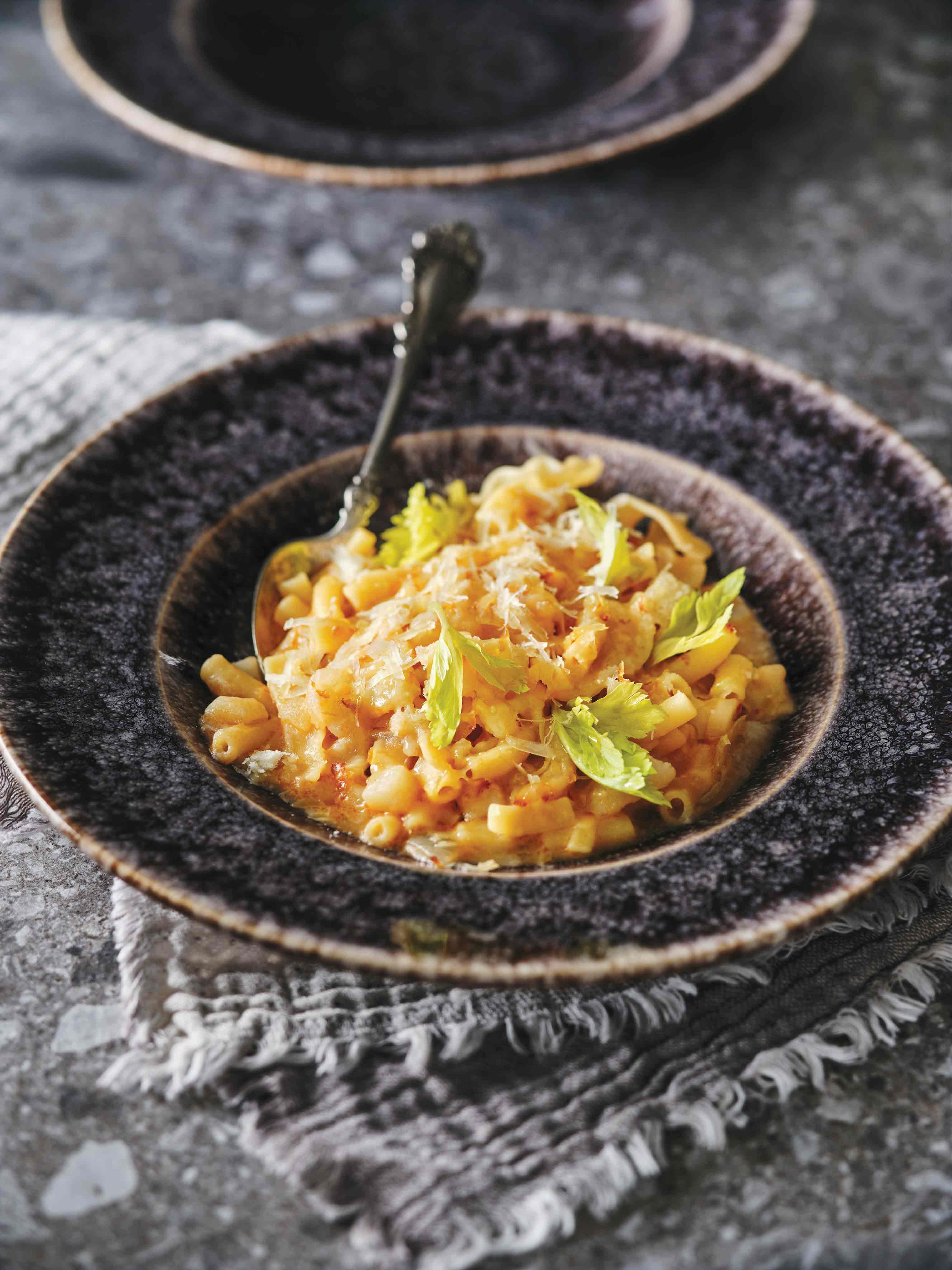 Pâtes de formes diverses et pommes de terre en cubes avec sauce dans un bol noir, garni de parmesan.