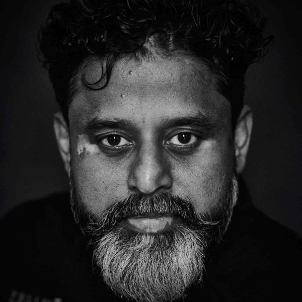 Portrait en noir et blanc d’un homme indien aux cheveux courts et bouclés et à la barbe grisonnante qui regarde l’appareil photo.