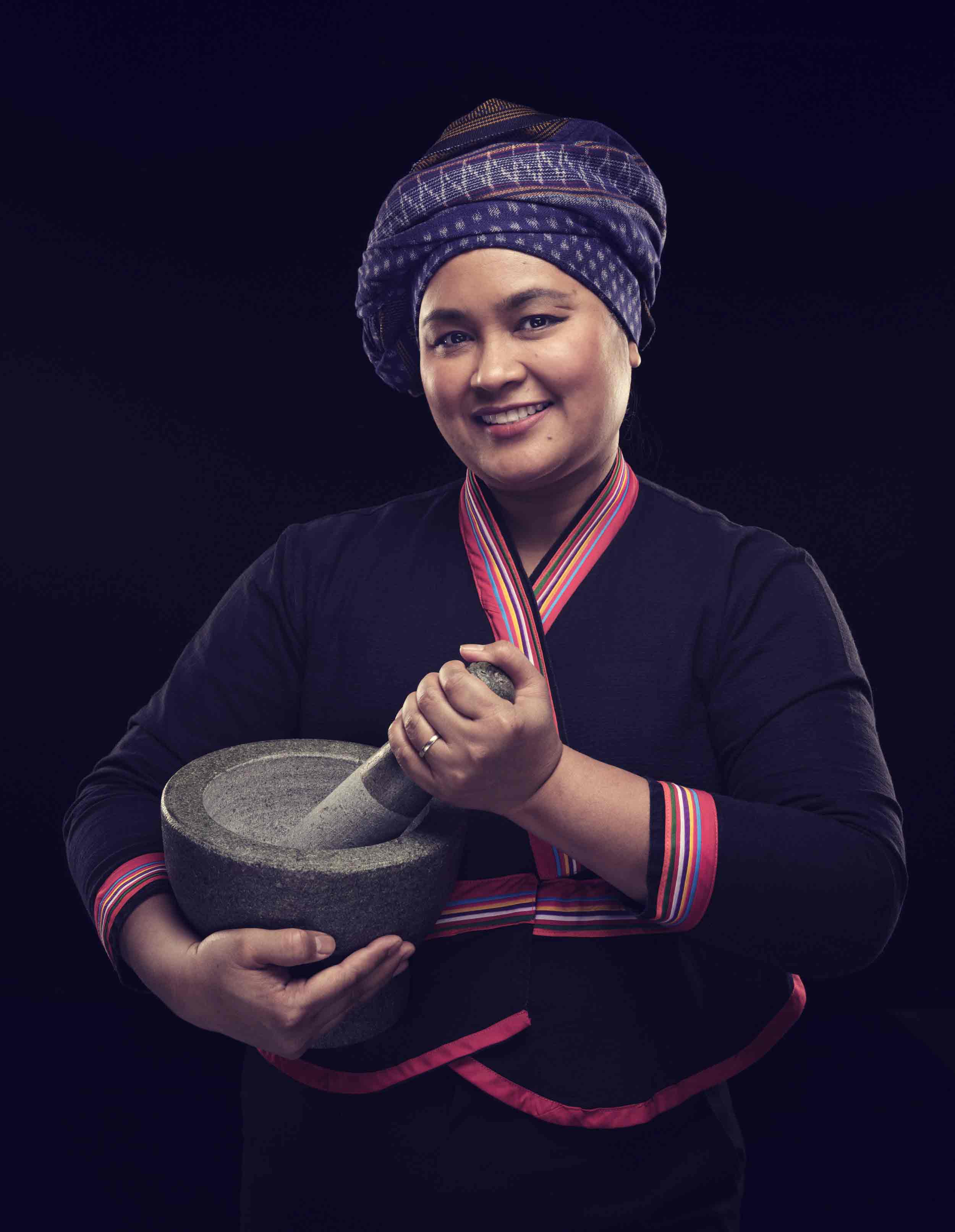 Portrait d’une femme thaïlandaise souriante portant un bandeau traditionnel et tenant un mortier et un pilon gris.