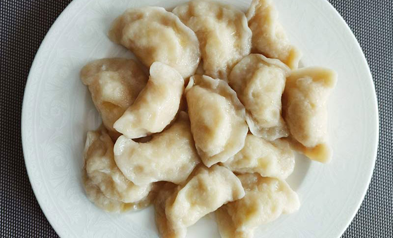 Pierogis servis sur une assiette blanche, vus en plongée.