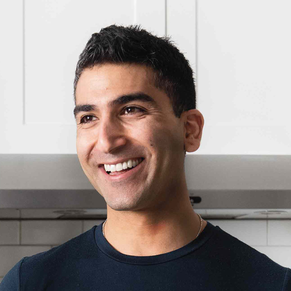 Un jeune homme souriant d’origine égyptienne plie de la pâte dans une cuisine blanche et lumineuse.