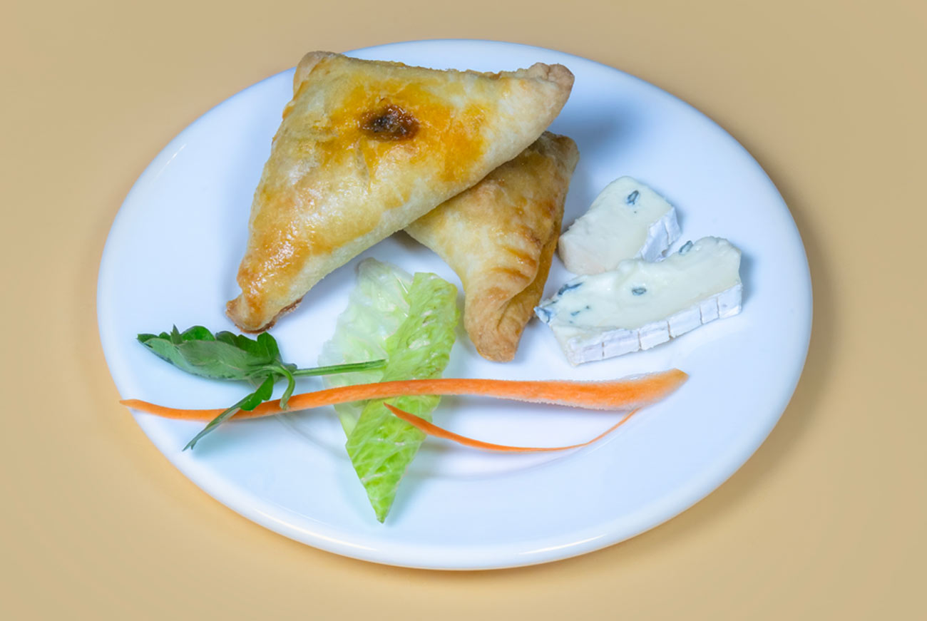 Une assiette blanche contenant deux ukajas dorés, de minces bâtonnets de carottes, une feuille de laitue, un brin de persil et deux tranches de fromage blanc.