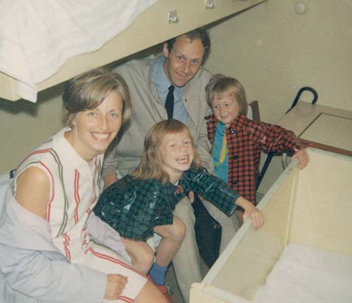 Famille de quatre personnes souriant à la caméra, assise sur un lit de fond à bord du SS Maasdam.