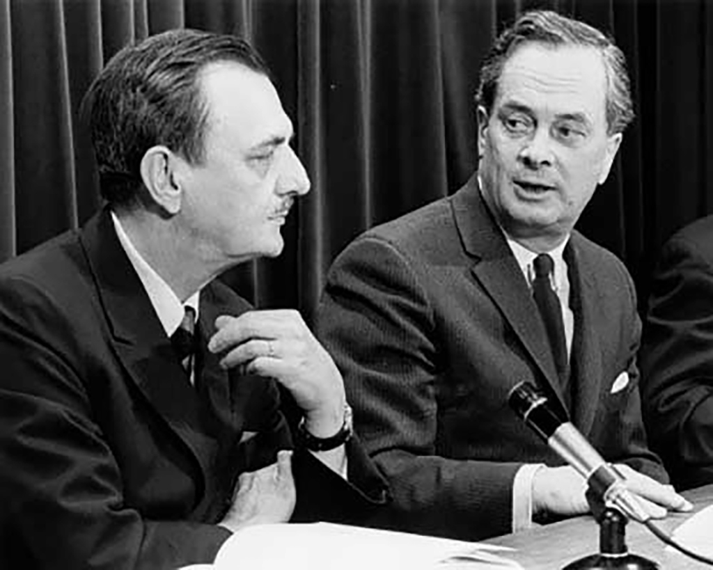 Photo d’archives de deux hommes en costume assis devant un microphone.