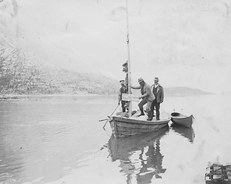 Trois hommes sont debout dans un bateau; il y a un petit bateau dans l’eau à côté.