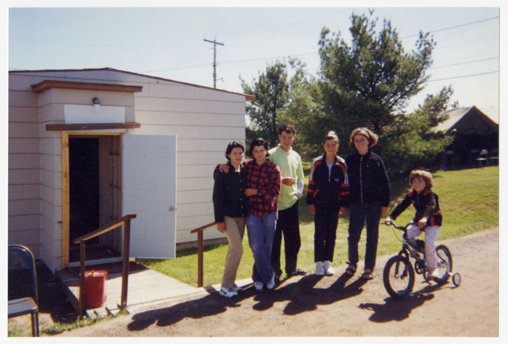Plusieurs personnes, ainsi qu’une fille sur un vélo, sont regroupés devant un bâtiment blanc.