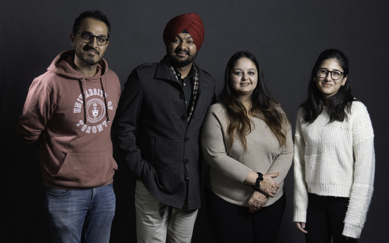 Quatre Sud-Asiatiques : deux hommes, l’un portant un turban, et deux femmes, debout devant un arrière-plan gris foncé.