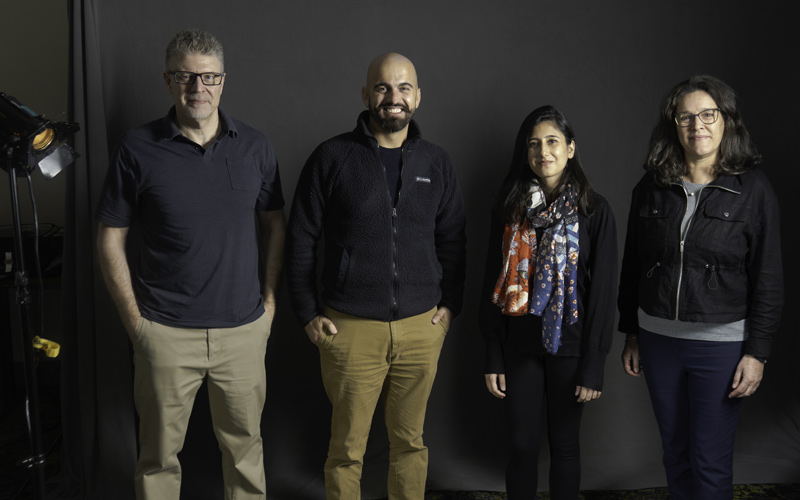 Homme blanc, homme syrien, femme pakistanaise, femme blanche-latina debout sur fond gris, à côté d’une lumière de studio.
