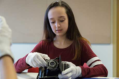 Une jeune fille portant des gants regarde l’appareil photo qu’elle tient.