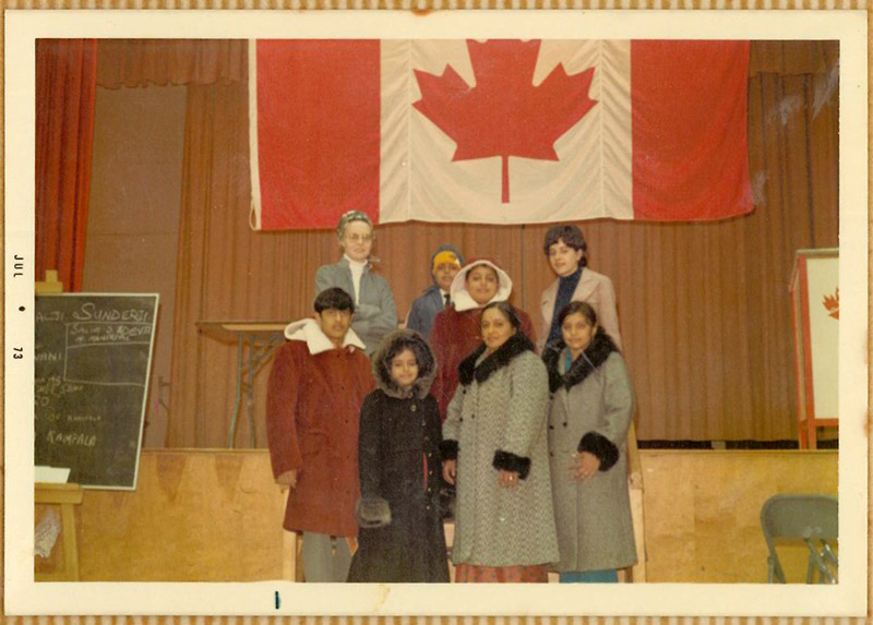Une famille portant des vêtements chauds d’hiver se tient devant un grand drapeau canadien accroché au mur.