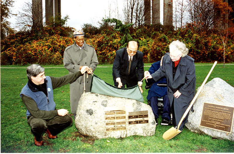 Quatre personnes soulèvent un revêtement d’une plaque, une pelle s’appuie contre la roche sur laquelle la plaque a été placée.