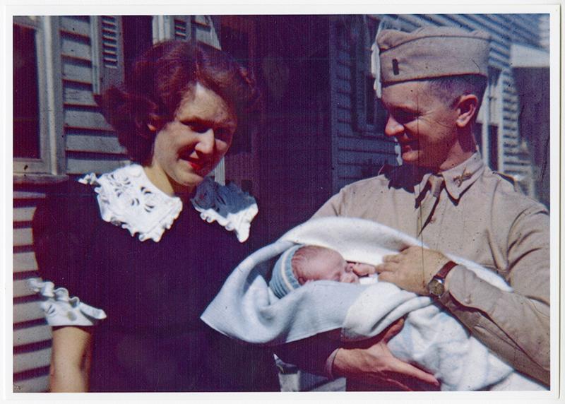 Une jeune femme en bleu debout à côté d'un homme en uniforme qui tient un bébé dans ses bras.