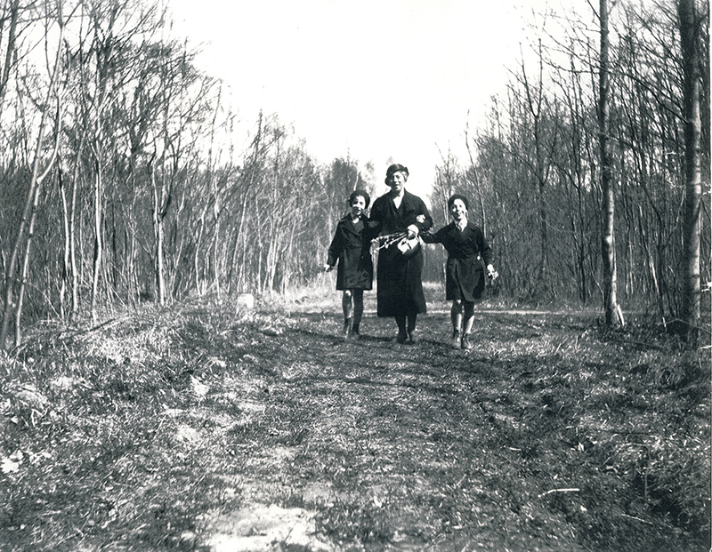 Une femme et deux enfants marchent joyeusement le long d’un sentier gazonné dans les bois.