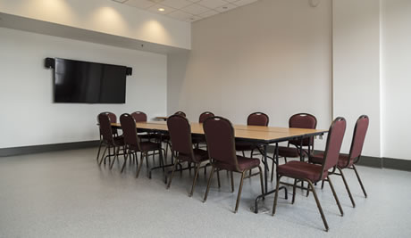 Une pièce dans laquelle se trouve une grande table entourée de douze chaises et un écran accroché au mur.