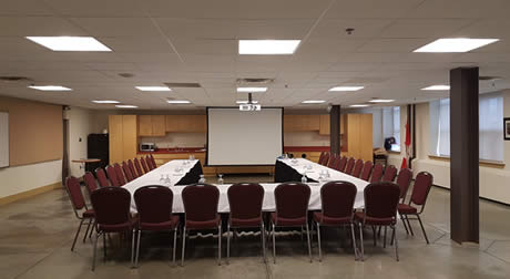Une pièce dans laquelle se trouvent trois tables placées en forme de U et un écran de projecteur accroché au mur.