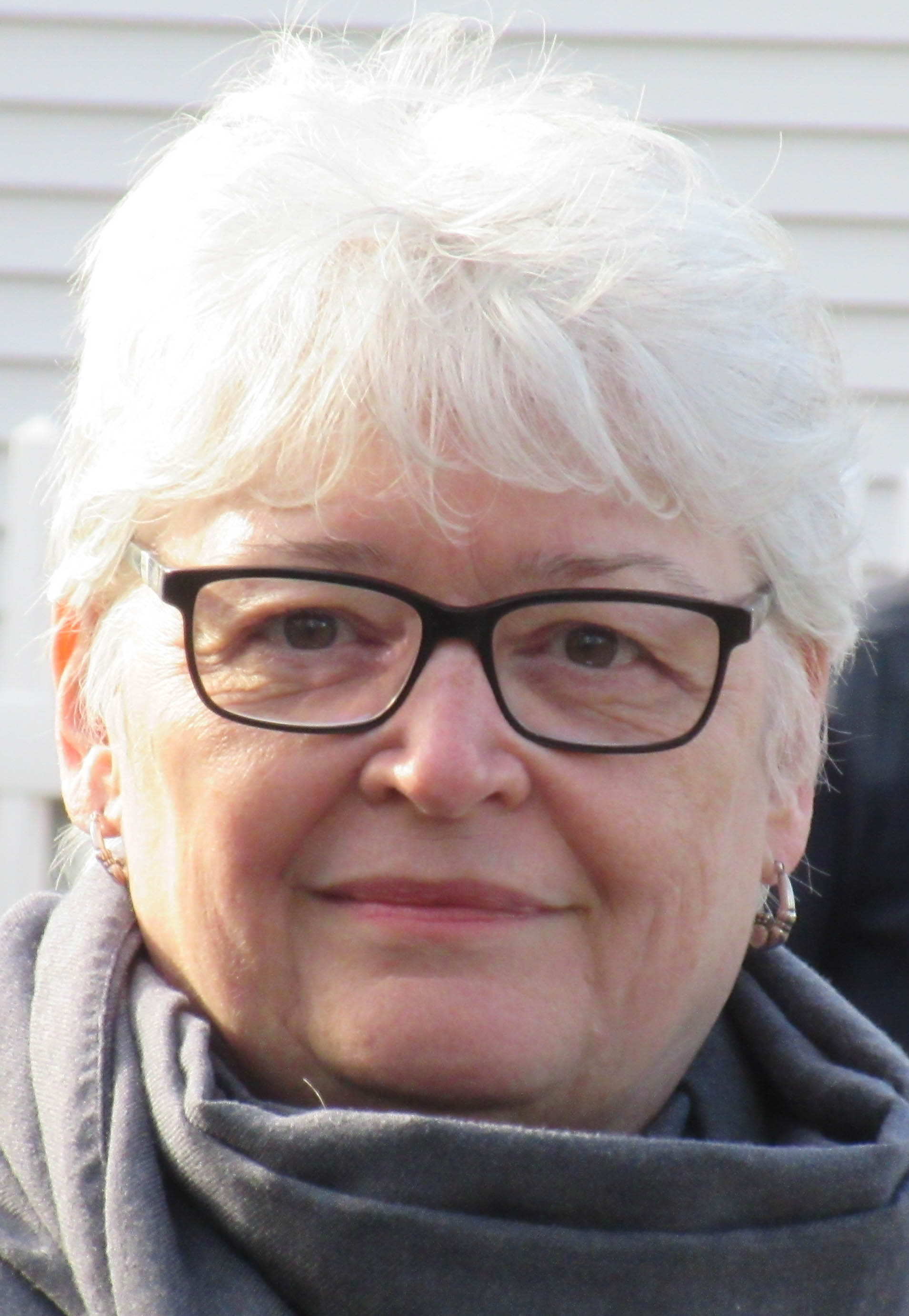Une photo de tête d’une femme avec des cheveux gris courts et des lunettes.
