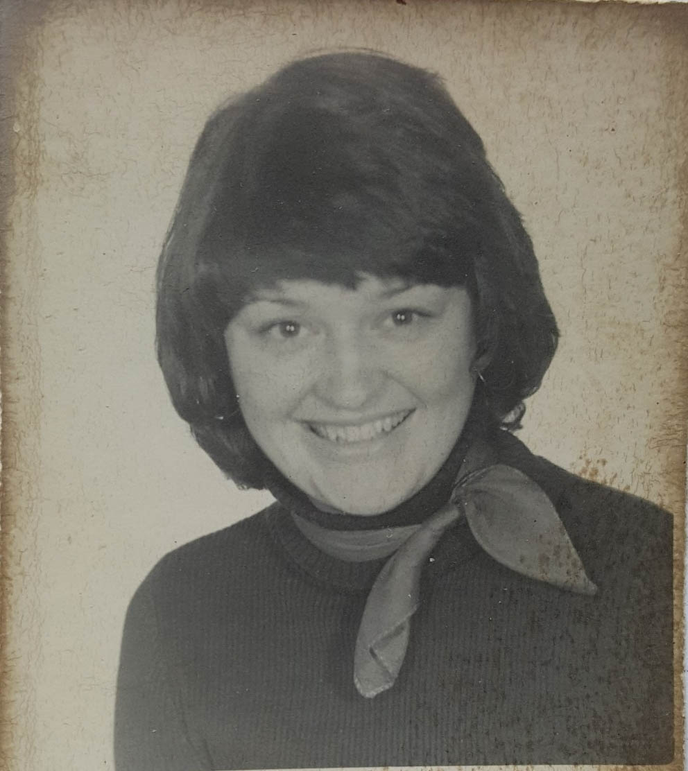 Une photo en noir et blanc, mouchetée et tachée, de la tête et des épaules d’une femme souriante.