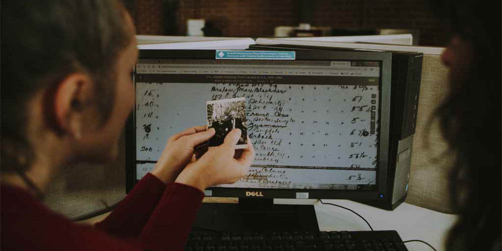 Une femme tient une photo en noir et blanc tout en regardant un écran affichant un vieux document manuscrit.