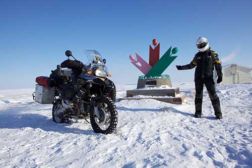 Une moto et un homme portant une habille de moto et un casque contre dans un terrain gelé.