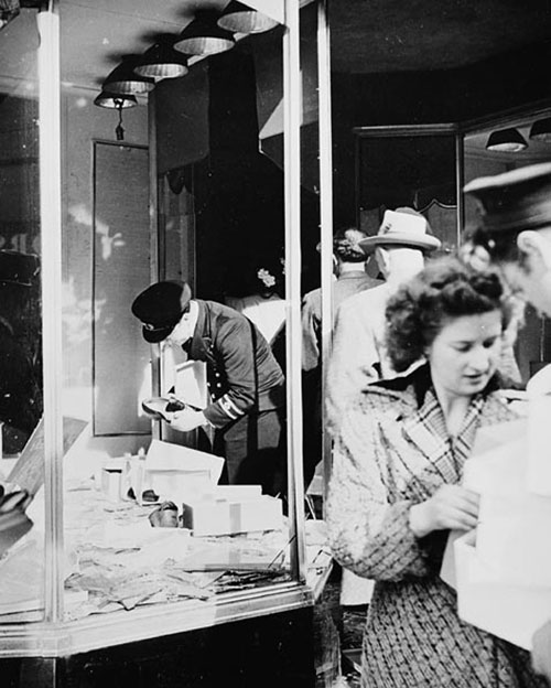 La vitrine d’un magasin aux fenêtres cassées, alors que des gens volent des boîtes de chaussures.
