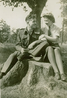 Un homme et une femme en uniformes militaires, assis bras dessus, bras dessous, sur une souche.