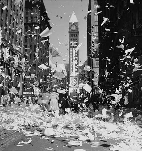 Une rue jonchée de papier et de confettis, avec une tour à horloge en arrière-plan.