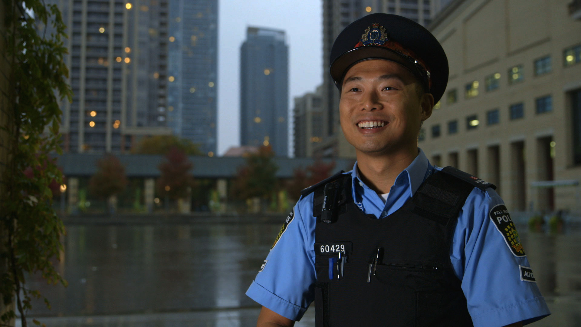 Un homme en uniforme de police, souriant, avec une rue urbaine en arrière-plan.