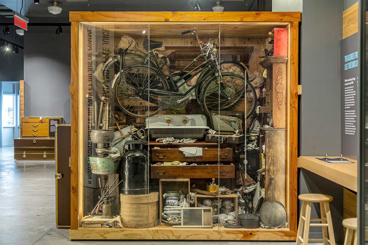 Une grande vitrine d’exposition remplie d’anciens objets, dont un vélo, une commode, un seau et un évier.