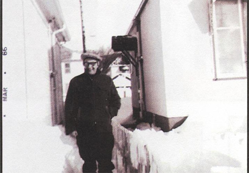 Une très vieille photographie d’un homme debout entre deux bancs de neige.