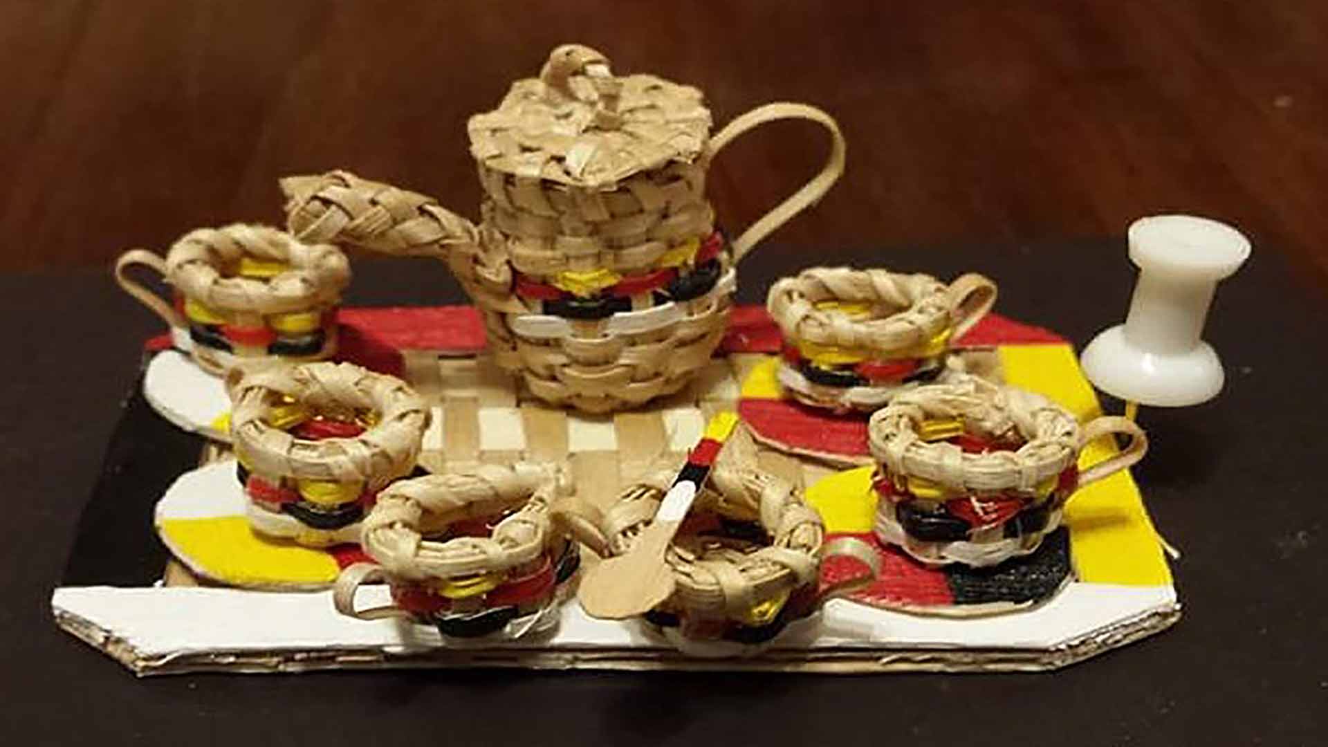 Un ensemble de six tasses de thé, chacune plus petite qu’une épingle de sûreté, et une théière miniature, le tout tissé à partir de bandes de bois.
