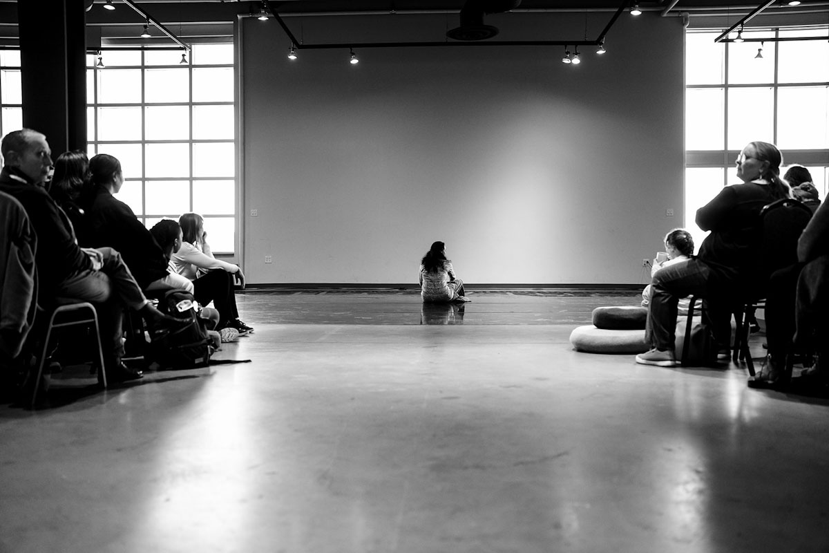 Une femme est assise par terre, face au public.