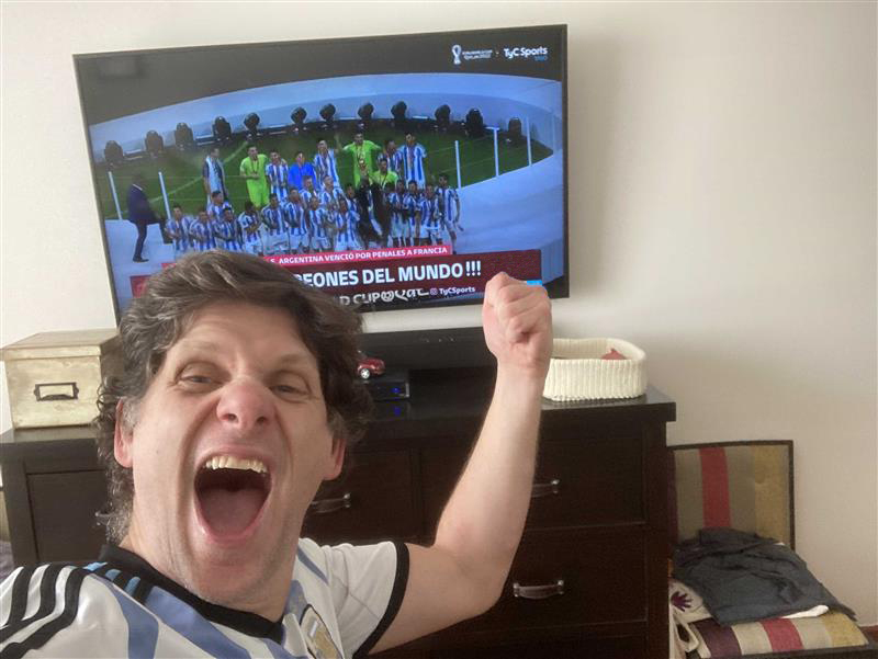Un homme applaudit devant une télévision montrant l’équipe de football argentine championne du monde en 2022.