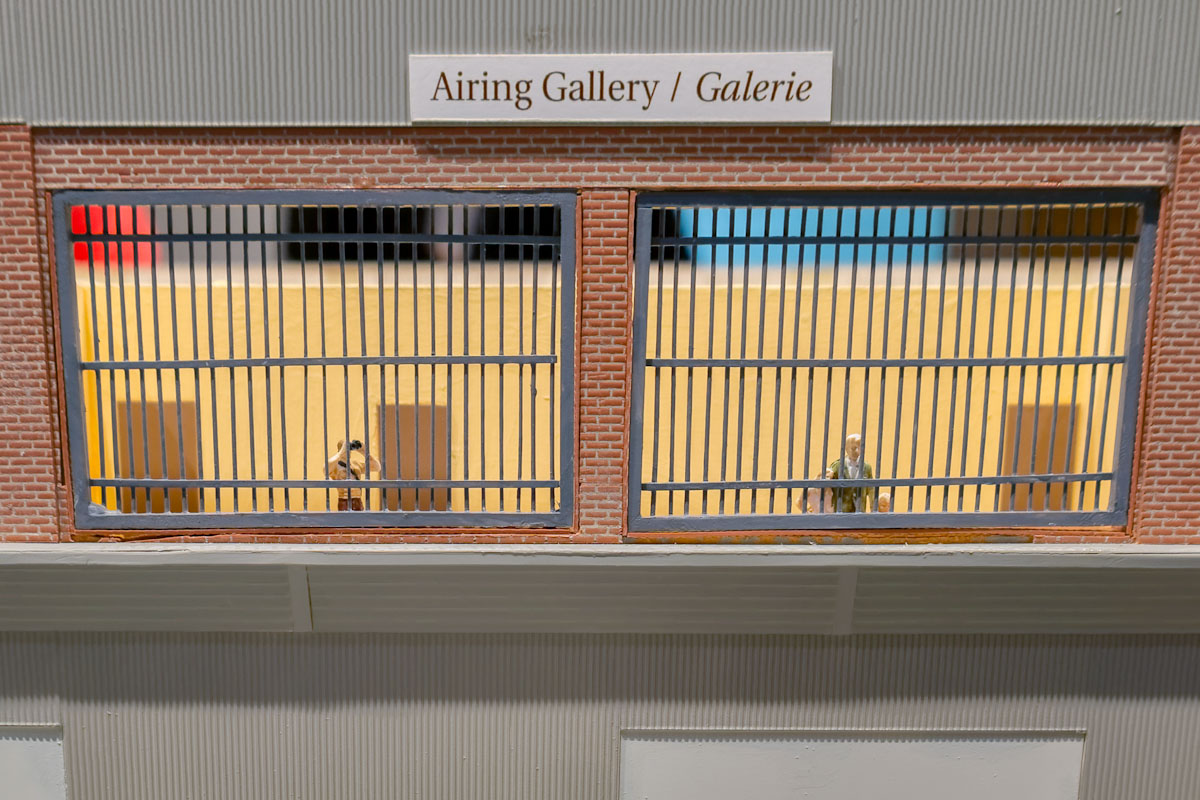 Figurines de deux hommes à la peau claire regardant derrière des barreaux métalliques au deuxième étage d’un bâtiment.