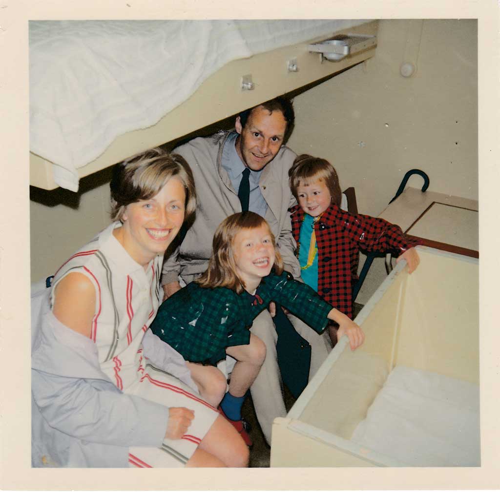 Un père, une mère et deux fillettes de moins de 10 ans, habillés en vêtements des années 1960, sont assis sur la couchette du bas dans une cabine de bateau bondée. Ils sont à l’étroit, mais ils sourient.