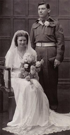 Une mariée est assise avec un grand bouquet de fleurs tandis que le marié se tient à côté d’elle.