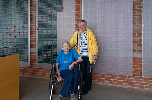 Une femme en fauteuil roulant est assise devant un mur couvert de plaques vertes.