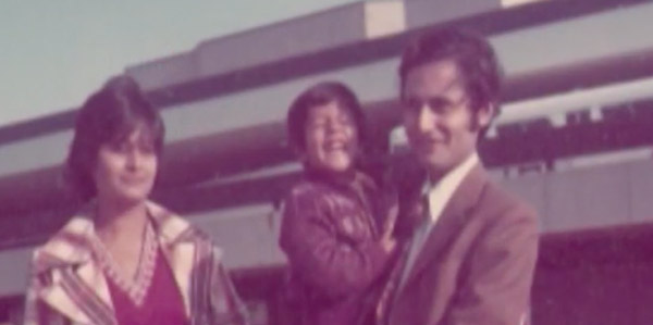 Photographie des années 70 d’une famille de trois personnes posant devant l’appareil photo à l’extérieur d’un aéroport.