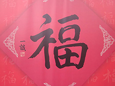 Un papier rouge de forme carrée sur lequel se trouvent des décorations en or entourant le caractère chinois « fu ».