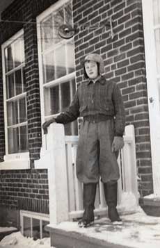 Une jeune personne portant un pantalon enfoncé dans des bottes d'hiver, des gants et un chapeau. Elle se trouve sur les marches avant enneigées d'une maison.