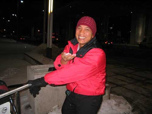 Un homme souriant portant un manteau rouge tient la neige dans sa main nue.