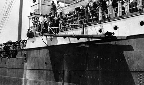 photo en noir et blanc d'un navire, avec des passagers alignés le long de la balustrade
