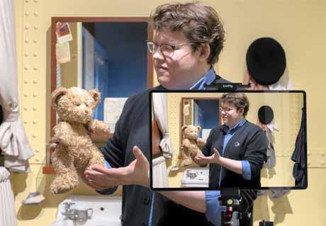 Un interprète tient un ours en peluche jaune pendant qu'il diffuse en direct un cours destiné à une classe à distance.