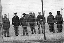 Image d’archives de plusieurs hommes debout derrière une clôture de barbelés.