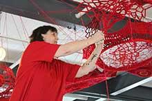 Un artiste travaille avec de la ficelle rouge pour créer un objet suspendu.
