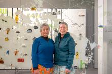 Deux femmes autochtones sourient devant leur installation d’art en verre.
